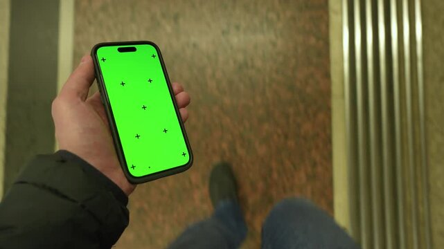 Pov view male hand holding modern smartphone keylight green screen gadget walking in street at night, camera locked on cell phone chroma key display, subway metro station, copy space