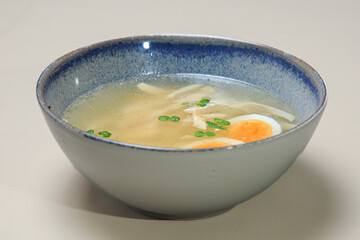 The image shows a bowl of clear broth-based soup, likely a chicken noodle soup. 