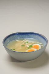The image shows a bowl of clear broth-based soup, likely a chicken noodle soup. 