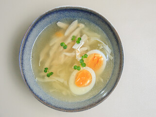The image shows a bowl of clear broth-based soup, likely a chicken noodle soup. 