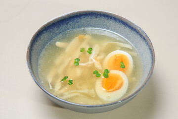 The image shows a bowl of clear broth-based soup, likely a chicken noodle soup. 