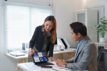 Professional Asian colleagues reviewing financial charts on digital tablet, collaborating in sleek contemporary workplace