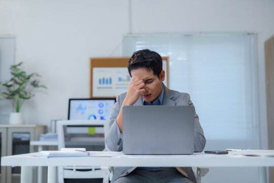 Exhausted professional experiencing work related stress, holding head while sitting at laptop in contemporary workspace, displaying signs of burnout