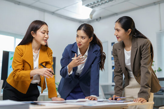 Professional asian businesswomen collaborating in conference room, reviewing financial graphs, exchanging strategic insights for corporate growth and teamwork
