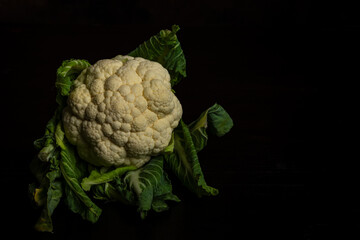 View of a white cauliflower with green leaves on a table and a dark background, horizontal with copy space