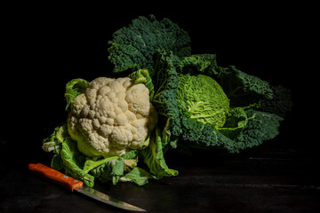 View of a white cauliflower, cabbage and knife on a table and dark background, horizontal with copy space