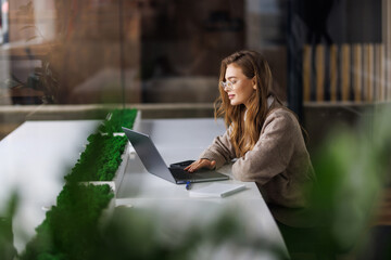 Business Woman working on a laptop in a modern office with greenery and coffee