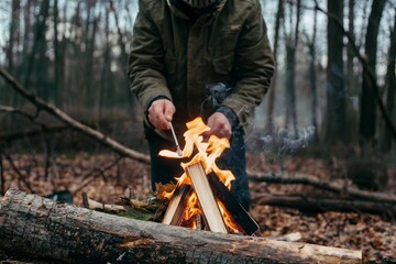 Hands build a cozy fire with logs and kindling in the woods during autumn afternoon