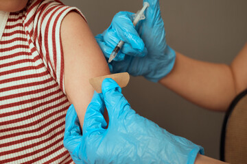 Fototapeta premium A young child is sitting comfortably in a clinic while a healthcare worker in blue gloves prepares to administer a vaccination. The child shows a calm demeanor, ready for the procedure
