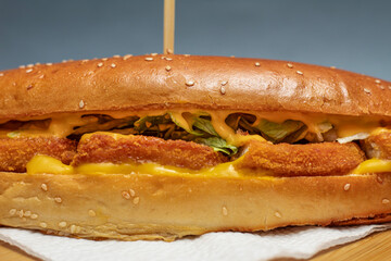 Crispy chicken sandwich in seasame hot dog bun on a wooden plate
