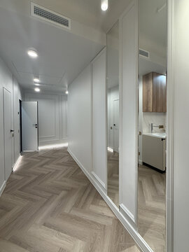 Bright hallway features sleek doors and subtle decorative wall elements. The flooring combines natural wood tones, while soft lighting creates a warm ambiance.