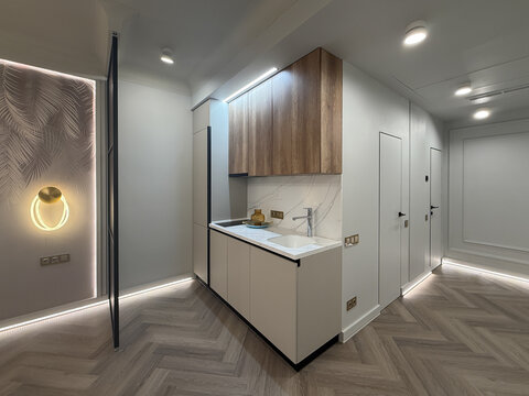 A contemporary apartment interior showcases a spacious layout with sleek wooden flooring and modern lighting fixtures. The kitchen area features minimalist cabinetry for a clean look.
