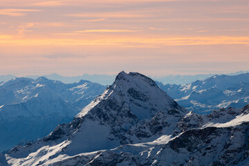 View of the Alpine mountain landscape at sunrise, when all the peaks are illuminated in shades of cyan, pink, and yellow