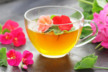 Scented geranium herbal tea in a glass cup with flowers on black kitchen background, closeup, stress healing drink, natural medicine and naturopathy concept