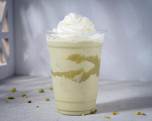 A rich and creamy pistachio frappé topped with whipped cream and drizzled with pistachio sauce, served in a clear plastic cup. A refreshing and indulgent frozen beverage perfect for pistachio lovers
