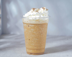 A creamy blended caramel frappé topped with whipped cream and a sprinkle of cinnamon, served in a clear plastic cup. A refreshing and indulgent cold coffee drink perfect for a sweet treat.