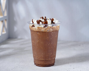 A rich and creamy chocolate frappé topped with whipped cream and drizzled with chocolate syrup, served in a clear plastic cup. A delicious frozen coffee beverage perfect for a sweet indulgence