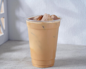A creamy iced coffee served in a clear plastic cup with ice cubes, showcasing a smooth and refreshing blend of espresso and milk. The minimalist café setting enhances the modern and stylish aesthetic
