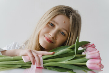 Naklejka premium Beautiful girl with blond hair with a bouquet of flowers. Girl in a bright room with a bouquet of tulips. Fresh spring flowers