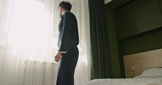 A young Caucasian man wakes up and falls back asleep. The man is tired and doesn't want to get out of bed in the morning.