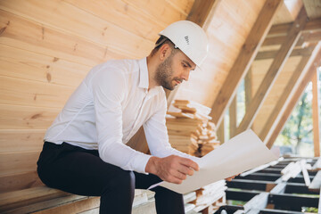 Architect wooden buildings. Man stands under frame wooden house. Man architect studies...