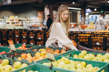 Woman choosing apples in supermarket with shopping cart