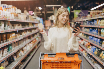 Young woman using smartphone and credit card while shopping in supermarket