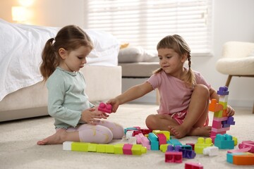 Obraz premium Cute little sisters playing with colorful building blocks on floor at home