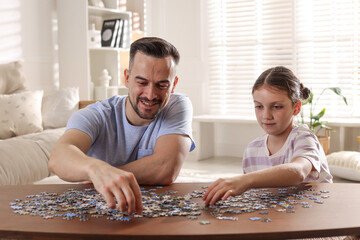 Fototapeta premium Happy father and his daughter solving puzzle together at wooden table indoors