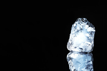 Piece of clear ice on black mirror surface, space for text