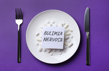 Cutlery near plate with pills and word Bulimia Nervosa on dark violet background, flat lay
