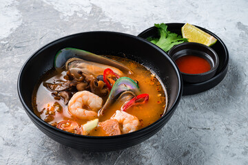 Traditional spicy Thai soup Tom Yum with shrimp and seafood in ceramic bowl on stone background