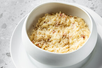 A creamy bowl of risotto topped with grated cheese and pepper, served on a stylish white plate. The dish appears appetizing against a light, textured background.