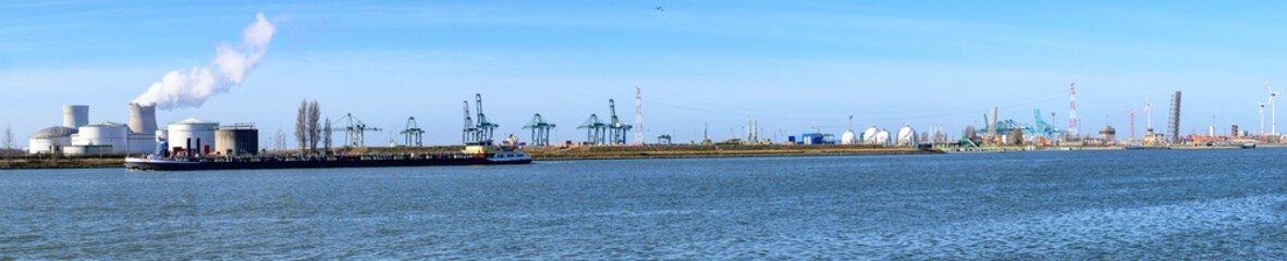 Obraz premium Industrial port panorama with cranes and smokestacks.