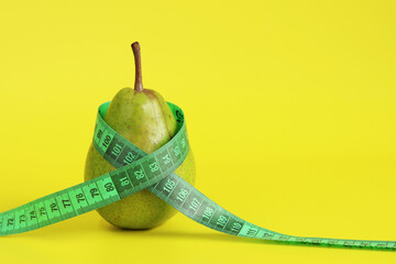 Measuring tape wrapped around a pear. Metaphor - figure like a pear. Ripe green pear and tape measure on yellow background. Concept of healthy eating, diet and weight loss. Volume and weight control