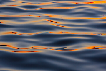 Gentle waves create a mesmerizing pattern on the water's surface, reflecting a warm sunset glow....