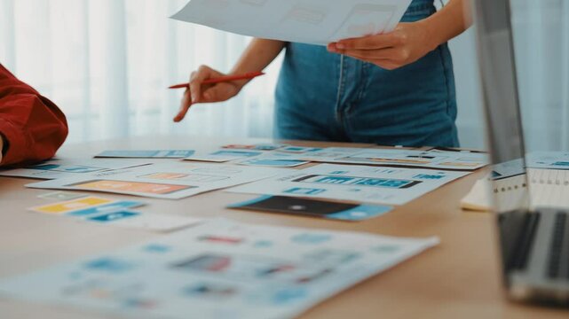 Excellent startup company employee presenting user interface prototype for mobile application to smart co-worker in office workspace. UX UI designer explain function of icon design on paper. Synergic