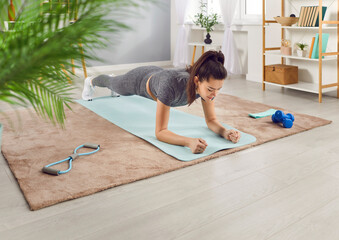 Slim athletic girl having fitness workout at home, doing plank exercise in the living room. Woman...