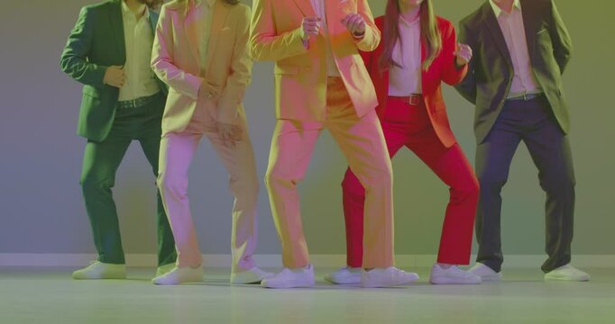Group of people in colourful suits dancing at disco party with flashing light. Low section shot, male and female dancers in bright clothes moving legs, feet doing synchronised shuffle on floor