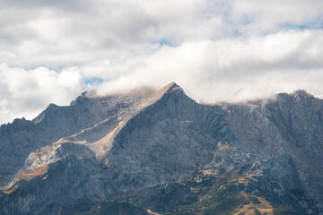 Beautiful view of rugged, majestic Alpspitze (Wetterstein) peak partially covered by clouds against a clear sky, creating a peaceful & inspiring nature scene perfect for outdoor, adventure, or travel 