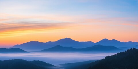 Fototapeta premium The mountains are shrouded in a thick layer of fog, creating a serene and peaceful atmosphere. The sky above is a stunning mix of warm oranges and cool blues, adding a touch of magic to the scene