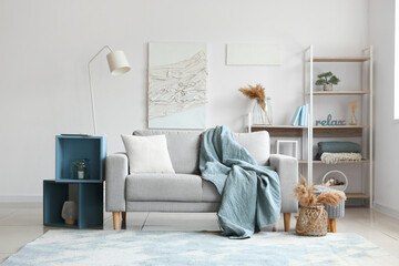 Obraz premium Cozy grey sofa with soft blanket, cushion and stylish shelves in interior of light living room