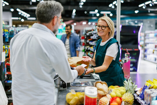 Customer paying with nfc technology on smartphone at supermarket while cashier is holding pos terminal