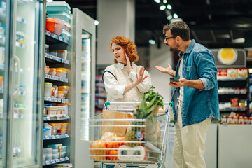 Couple arguing about grocery shopping in supermarket, woman refusing to buy something