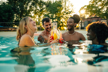 Friends toasting colorful cocktails in swimming pool at sunset