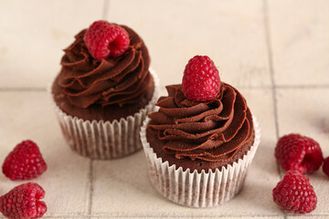 Tasty chocolate cupcakes with raspberries on white tile background