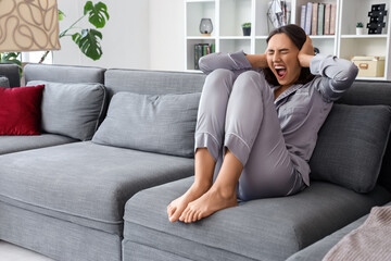 Obraz premium Beautiful young afraid woman sitting on sofa and screaming in living room