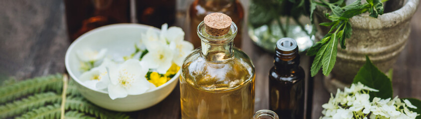 Herbal pure natural cosmetic ingredients on wooden background. Mix of holistic flowers and herbs, salt, massage herb-infused essential oil in glass bottles. Aromatherapy, fragrance production. Banner