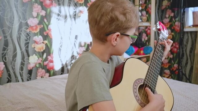 A teenage boy plays the guitar on the sofa. Active children's recreation. Let's learn to play the guitar.