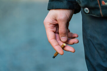Fototapeta premium Man smoking a cigar type of brown cigarette in a construction yard close up of arm holding the cigarette